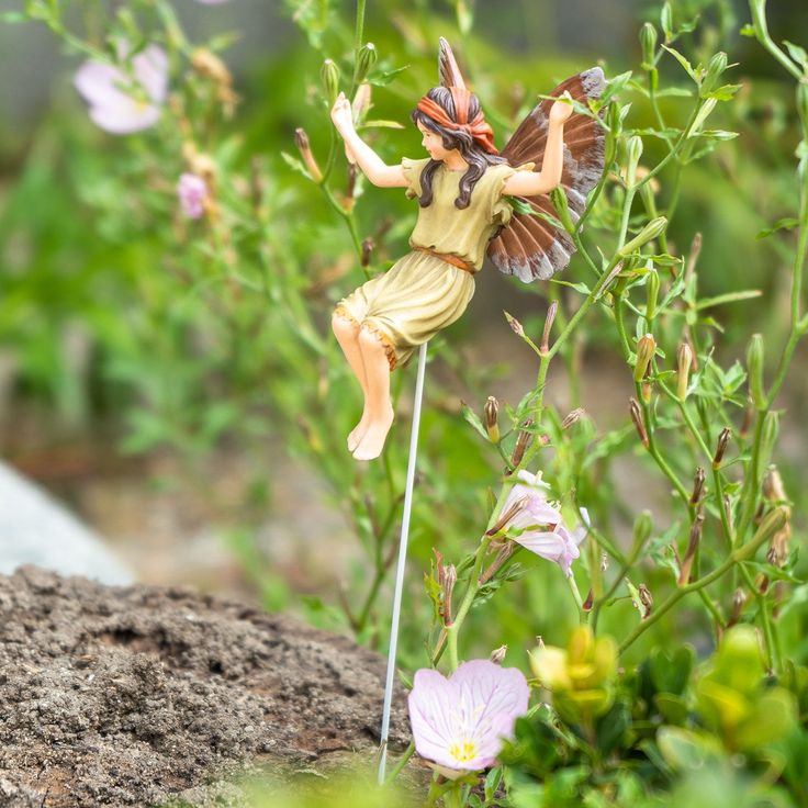 a fairy figurine sitting on top of a stick in the grass next to flowers