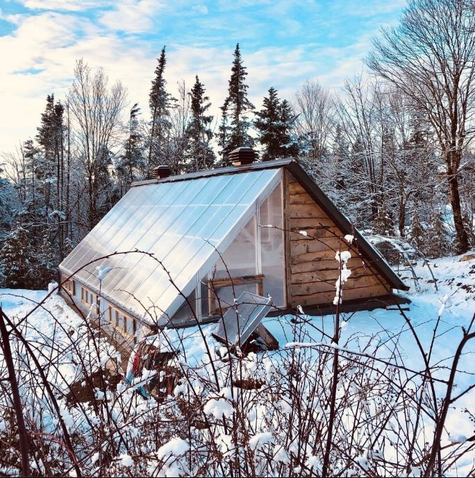 a small cabin in the middle of winter with snow on the ground and trees around it