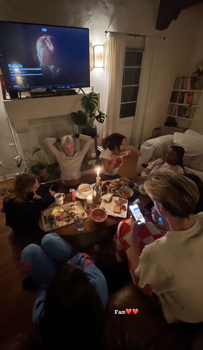 group of people sitting on couches watching tv in living room with food and drinks