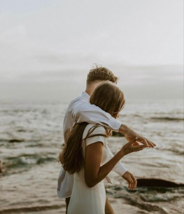 a man and woman are standing on the beach by the water looking at each other