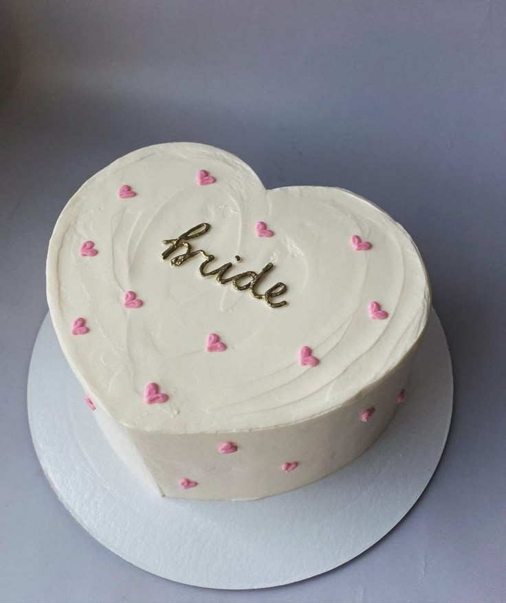 a white heart shaped cake with pink hearts on it and the word bride spelled in gold