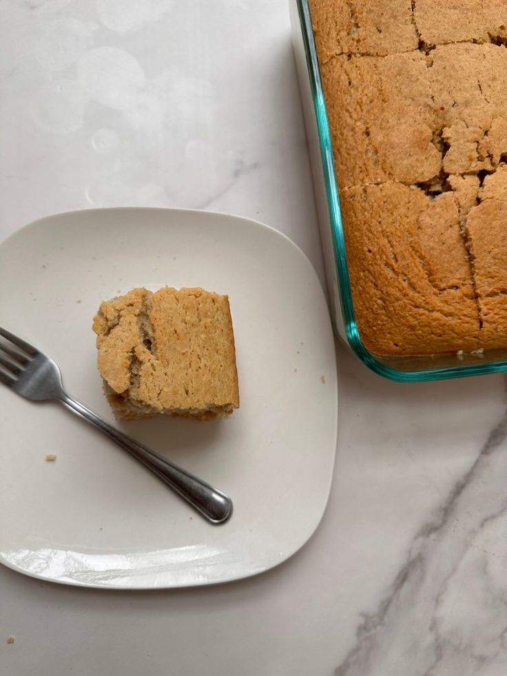 a piece of cake sitting on top of a white plate next to a loaf of bread