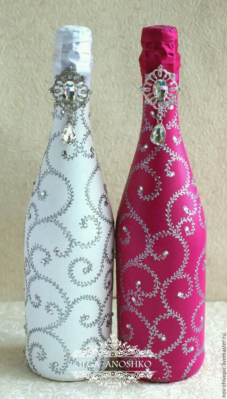 two wine bottles decorated with white and pink fabric, sitting side by side on a table