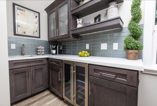 a kitchen with wooden cabinets and white counter tops, gray tile backsplash and wood flooring