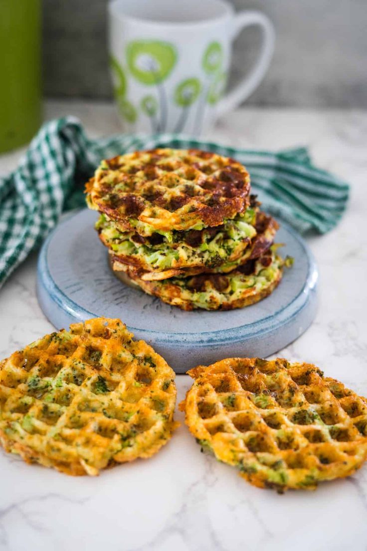 three waffles with broccoli and cheese on them next to a cup of coffee