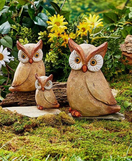 two owl figurines sitting on top of a log in the middle of a garden