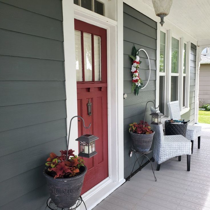 two buckets with flowers are on the porch next to a red door and chair