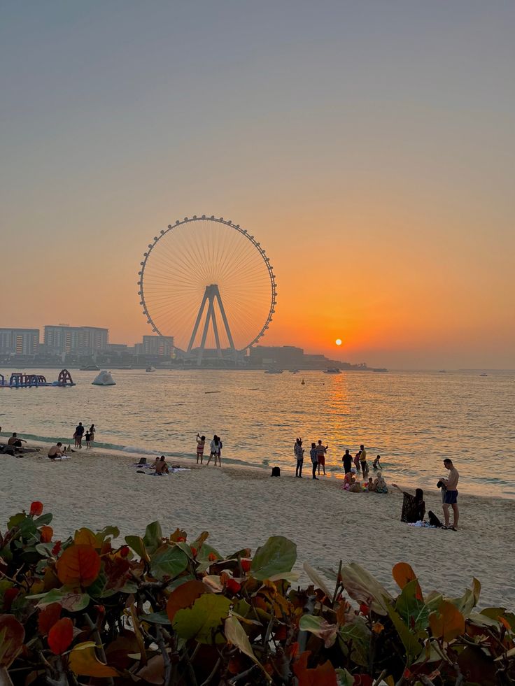 the sun is setting at the beach with people on it