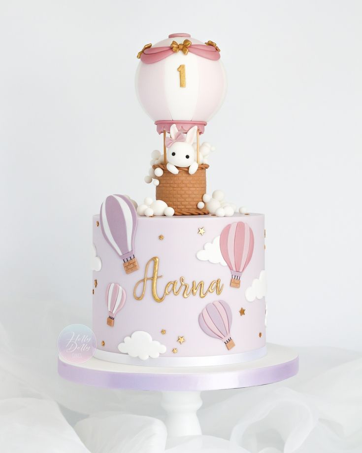 a pink cake with an animal on top and hot air balloons in the sky above it