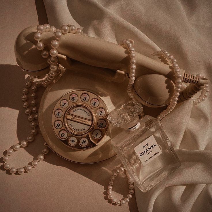 an old fashioned phone sitting on top of a bed next to a bottle of perfume