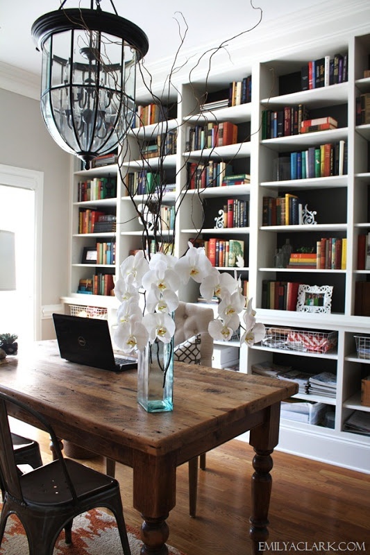 a laptop on a wooden table in front of a book shelf filled with lots of books