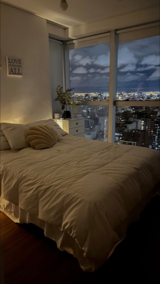 a bedroom with a large window overlooking the city at night, and a bed in front of it