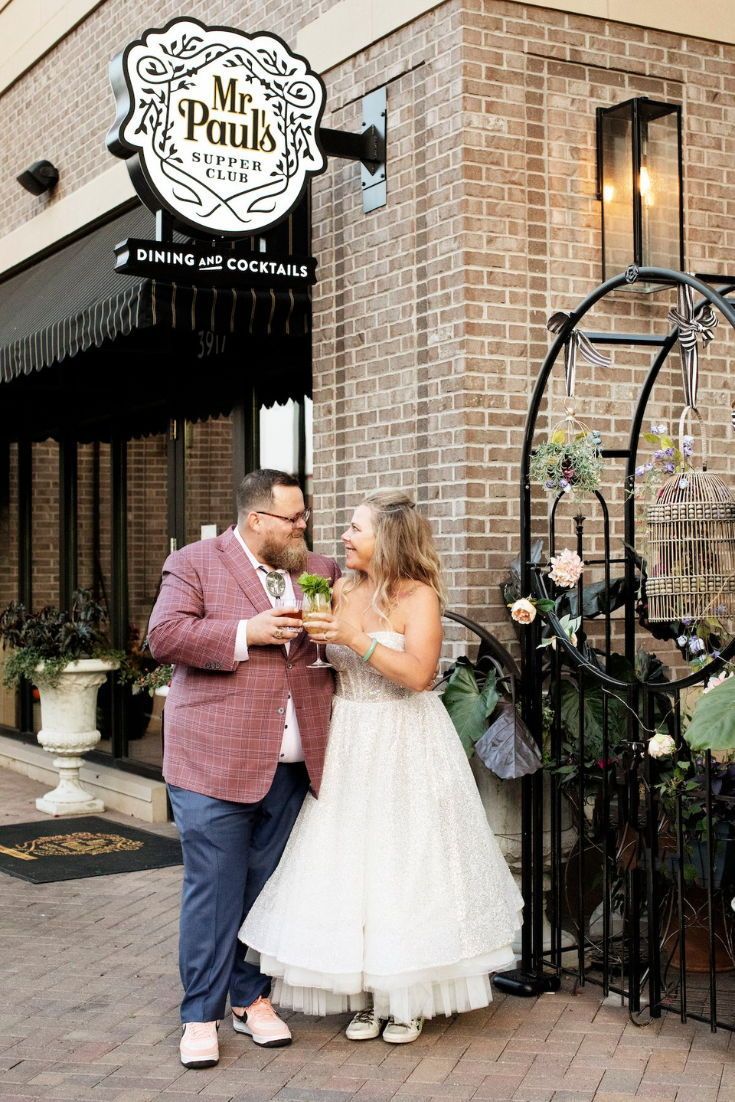 a man and woman standing next to each other in front of a building with flowers