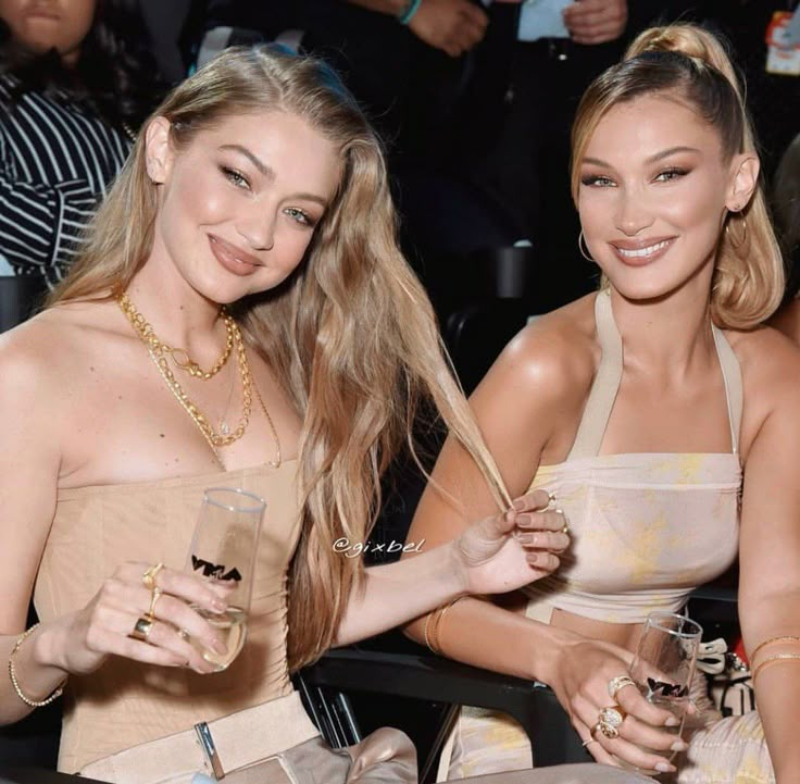 two beautiful young women sitting next to each other holding wine glasses in front of them