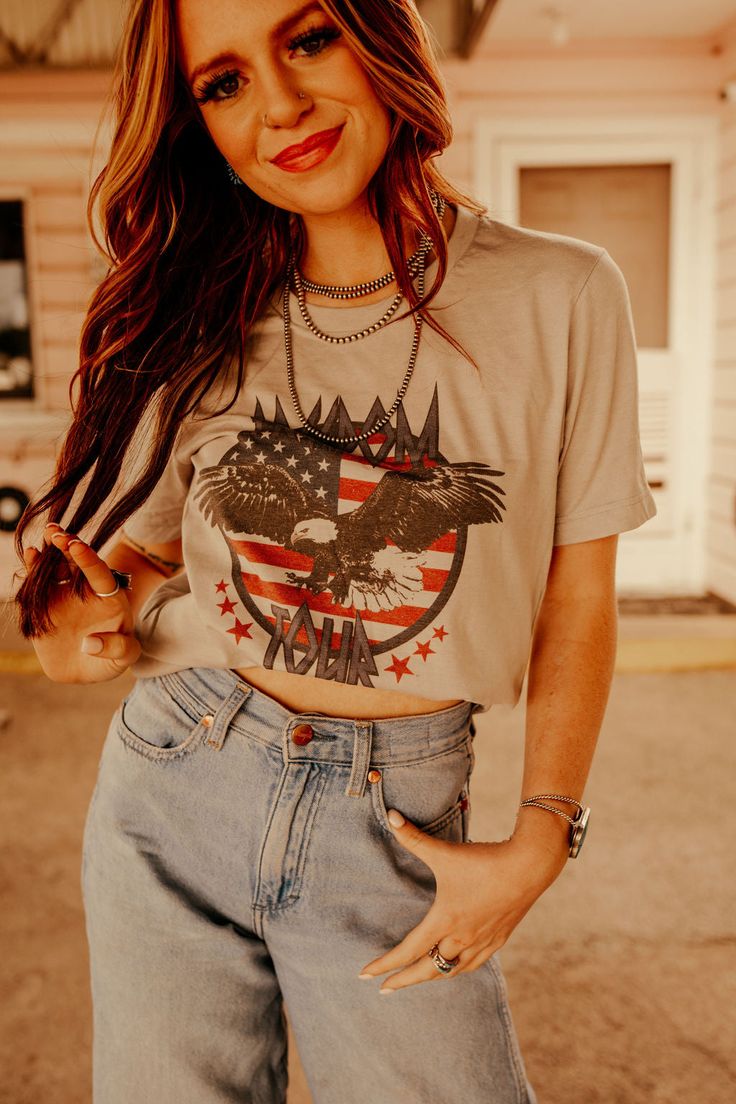 a woman with long hair wearing jeans and a t - shirt that has an eagle on it