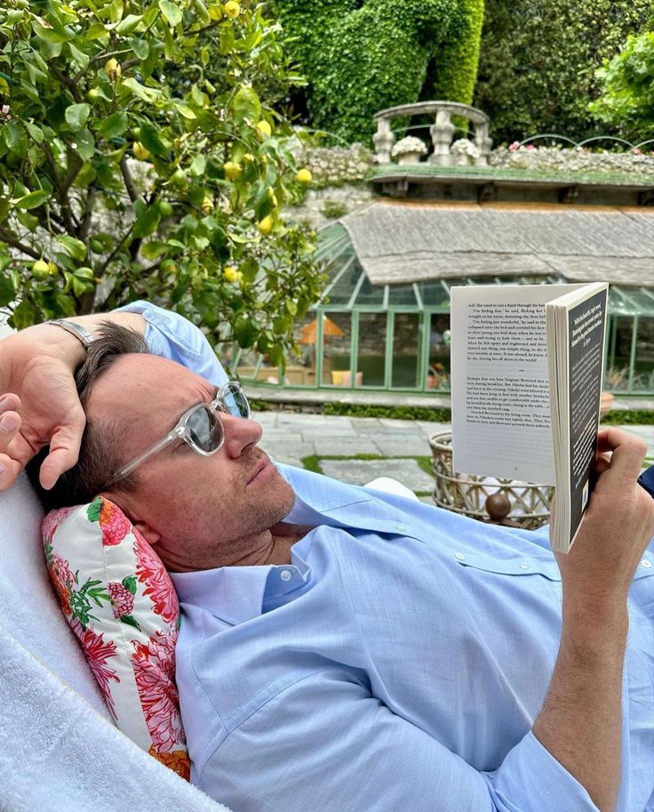 a man laying in a hammock reading a book while holding his head up