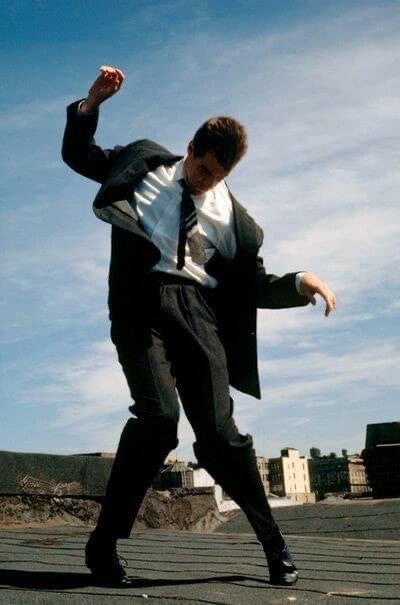 a man in a suit and tie is doing a trick on a skateboard outside