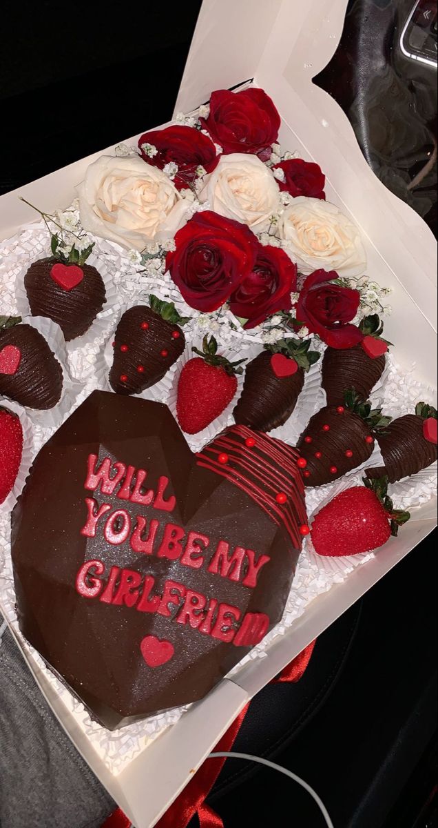 a heart shaped chocolate cake with strawberries and roses on the top is in a box