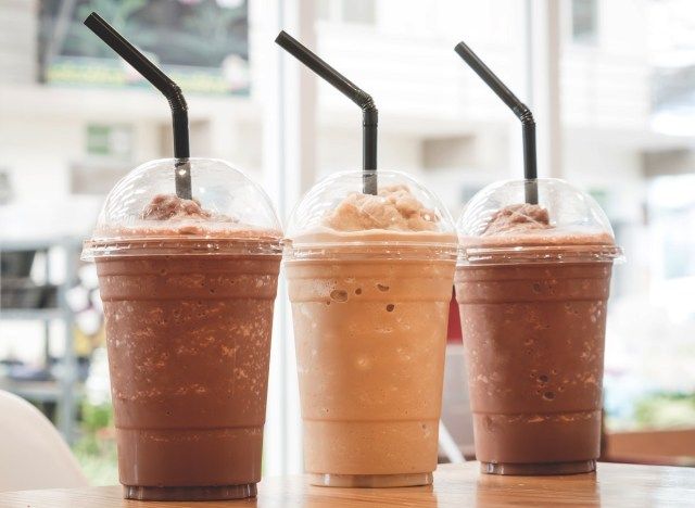 two drinks with straws and ice cream in plastic cups on a table next to a window