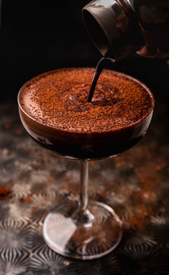 a person pours coffee into a chocolate drink in a wine glass on a table