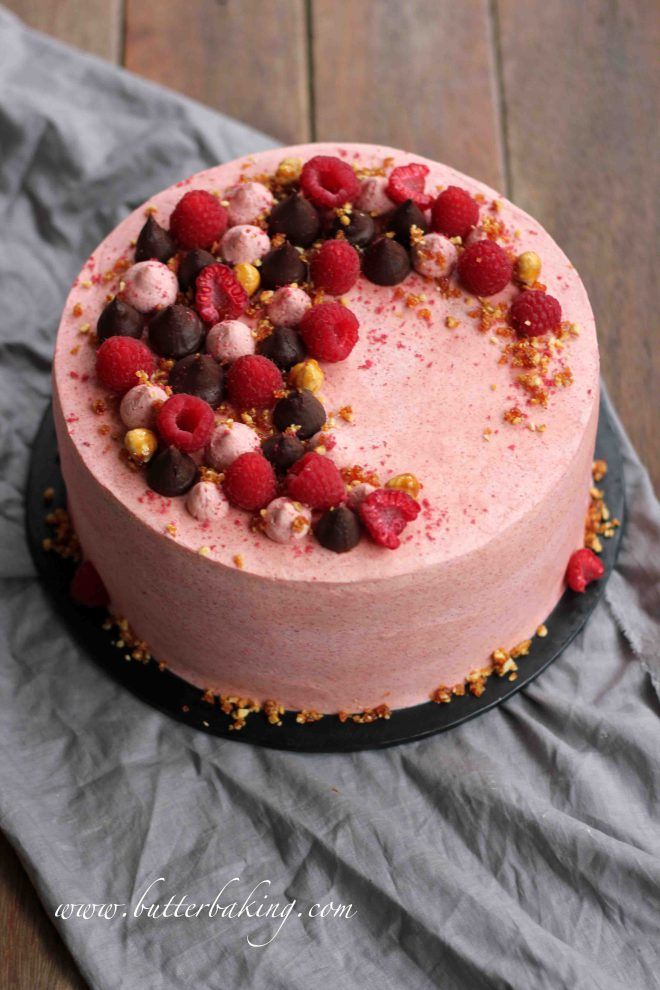 a cake with raspberries and chocolate chips on top sitting on a wooden table