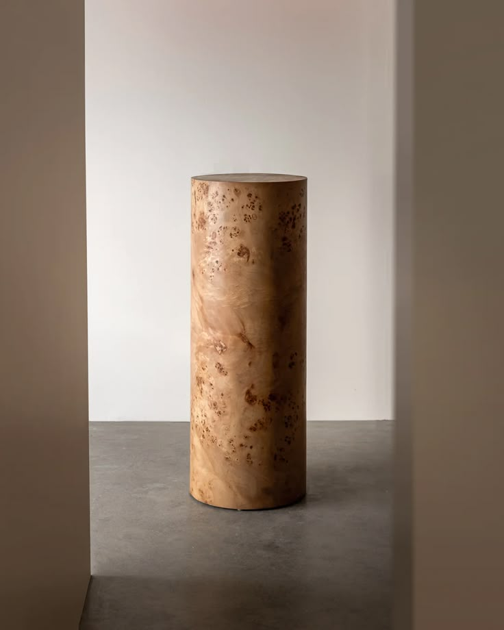 a round wooden table sitting on top of a cement floor next to a white wall