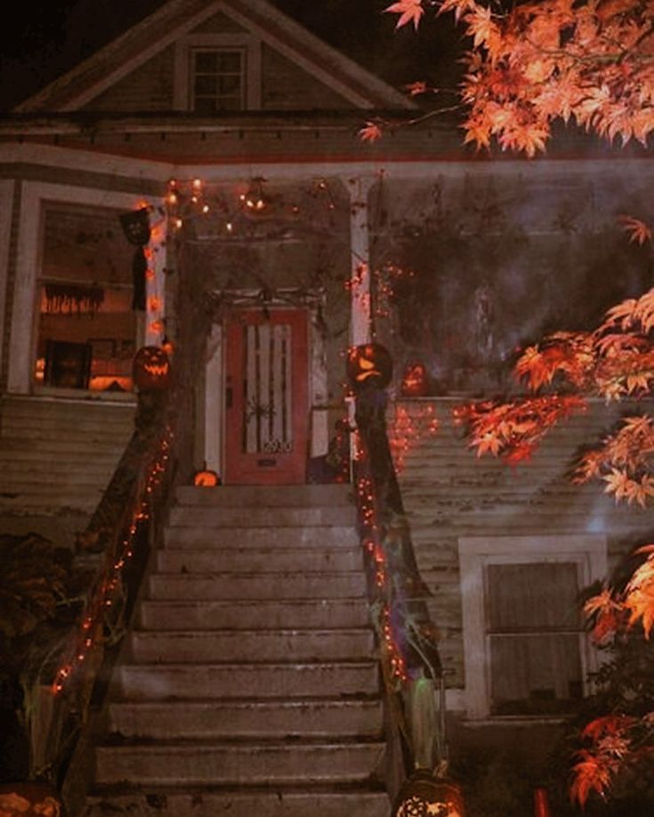 a house is lit up for halloween with pumpkins on the steps and trees in front