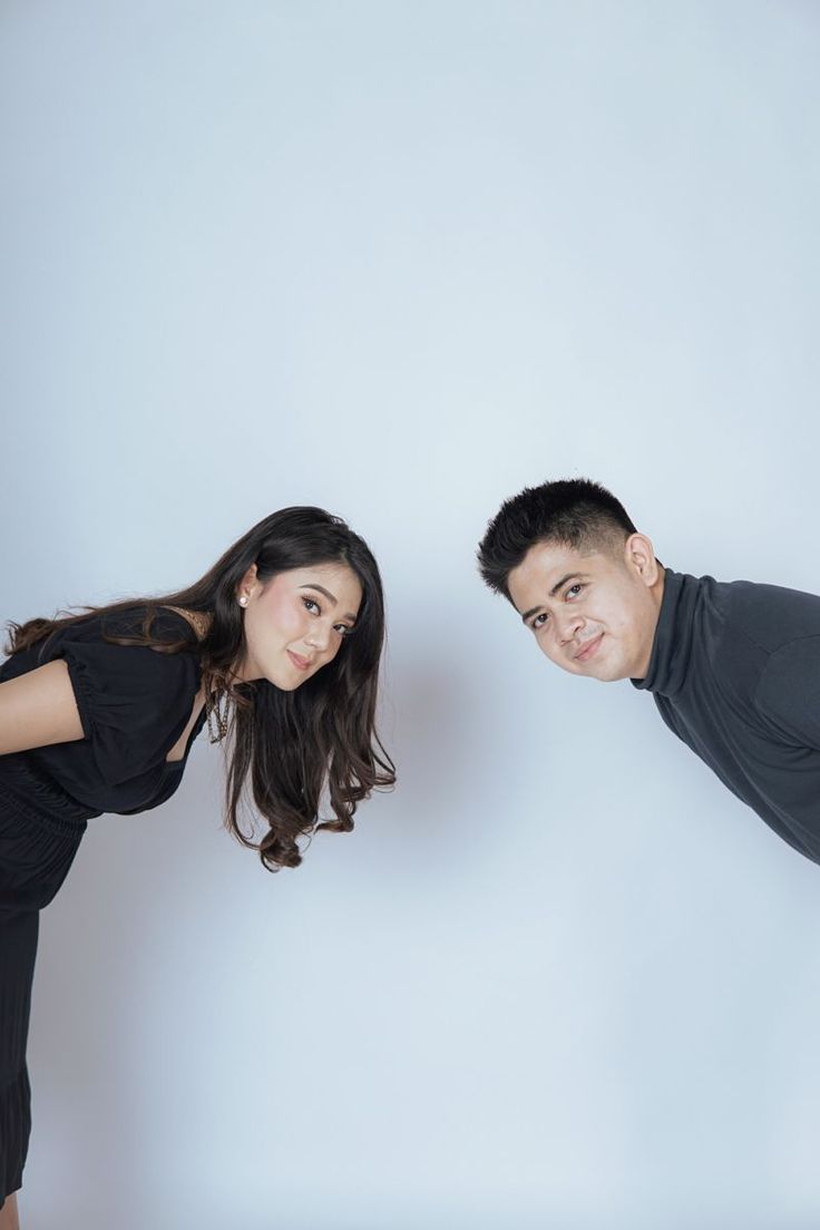 a man and woman are posing for a photo in front of a white background with their arms around each other