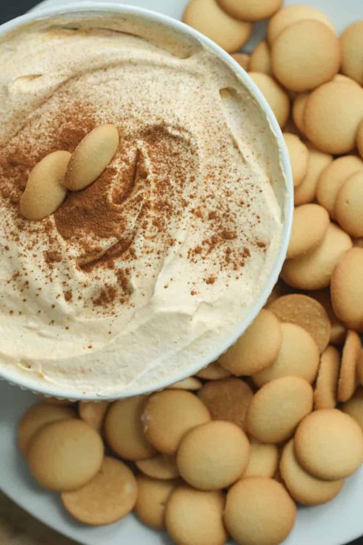 a white plate topped with lots of cookies next to a bowl filled with whipped cream