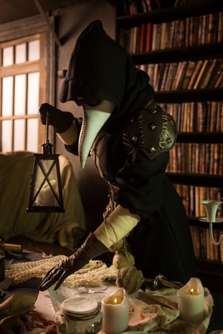 a person in a black outfit and hood is holding a lantern above a table with candles on it