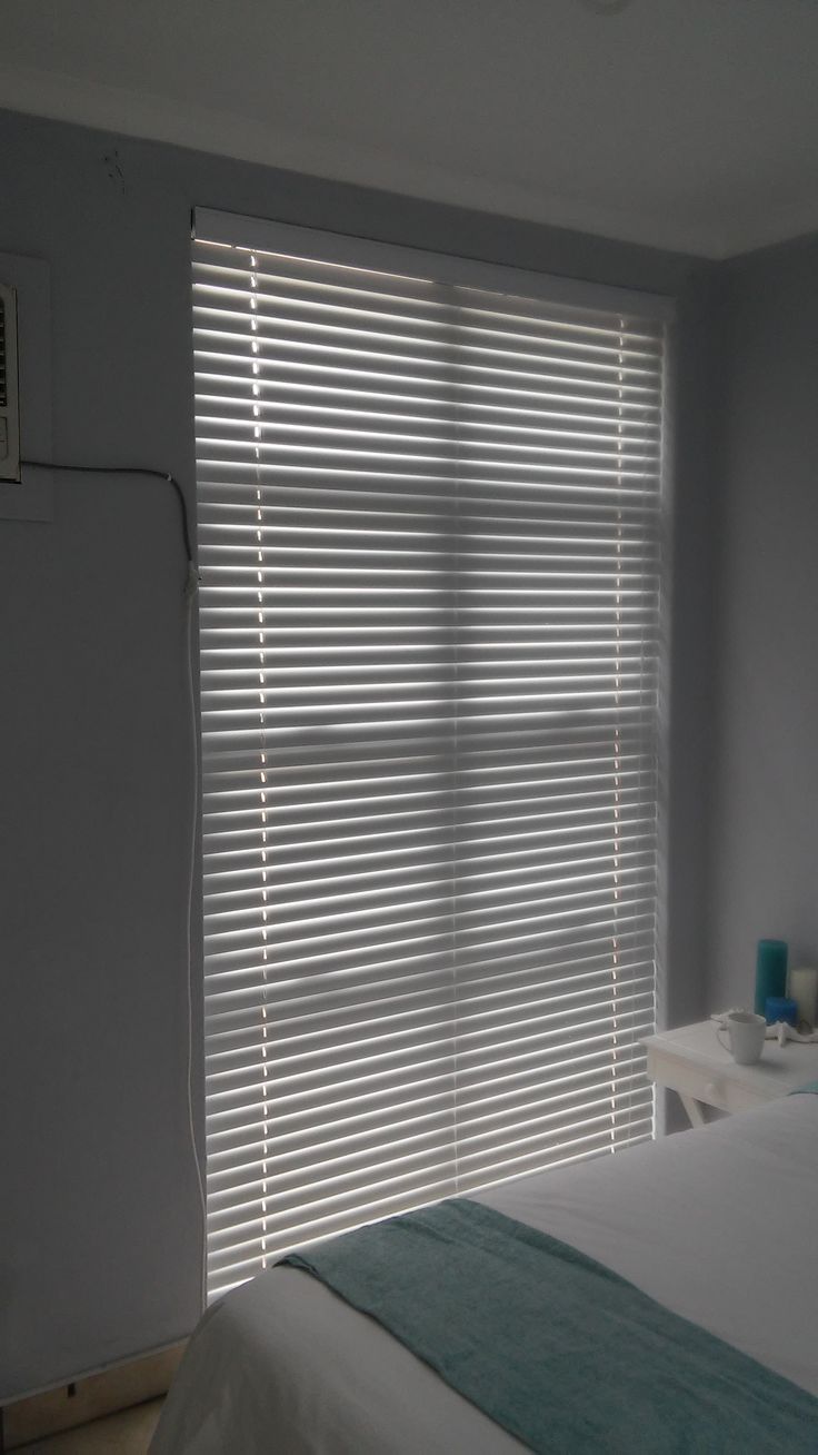 a bedroom with white walls and blinds in the window, along with a bed that has a blue blanket on it