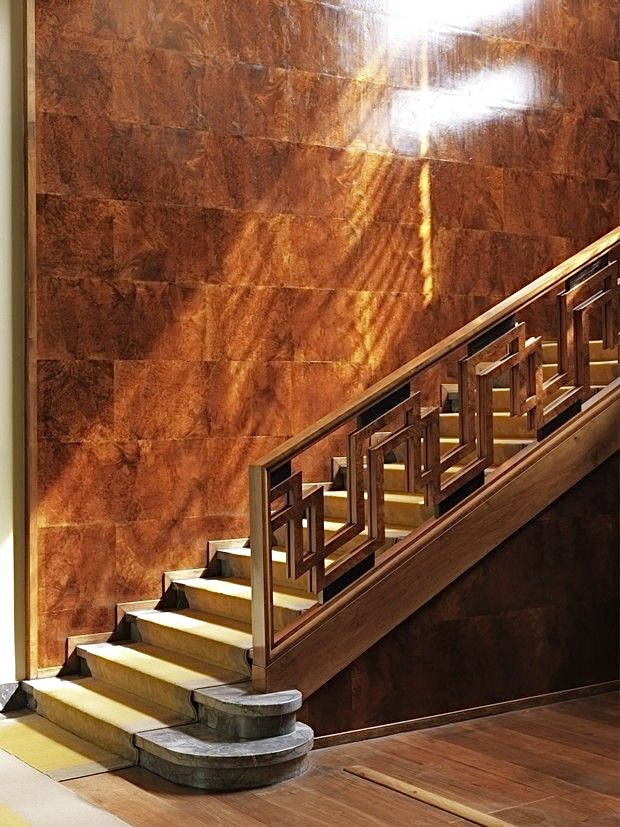 a wooden stair case next to a set of stairs in front of a wall with light coming through it