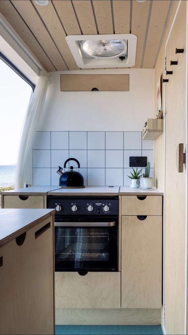 a kitchen area with an oven, sink and counter top next to a window that looks out onto the ocean