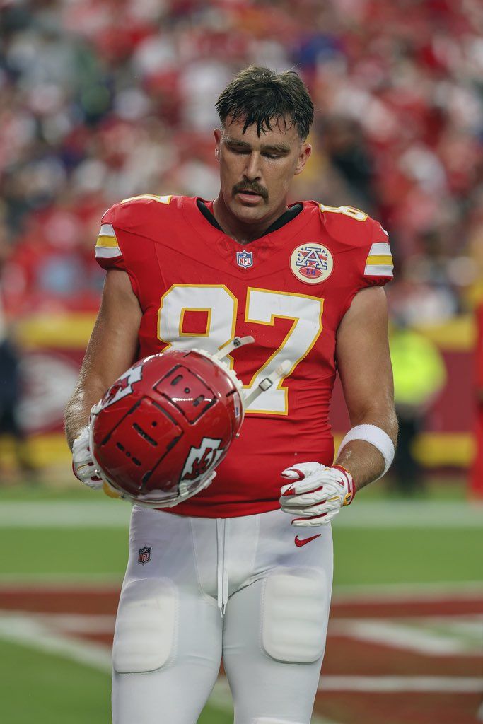 a football player holding a ball in his hand on the sidelines during a game