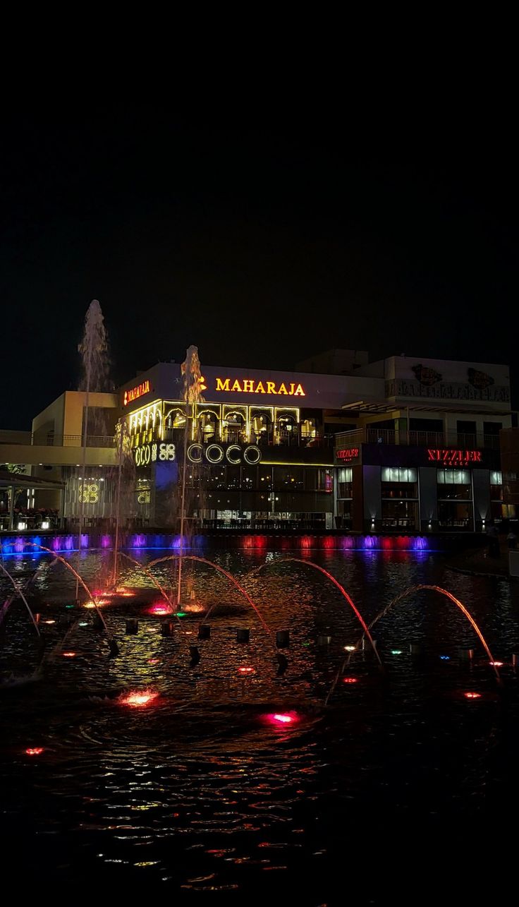 there is a fountain in the water with lights on it and people standing around watching