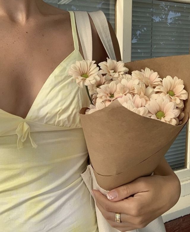 a woman in a white dress holding a bouquet of daisies on her left hand