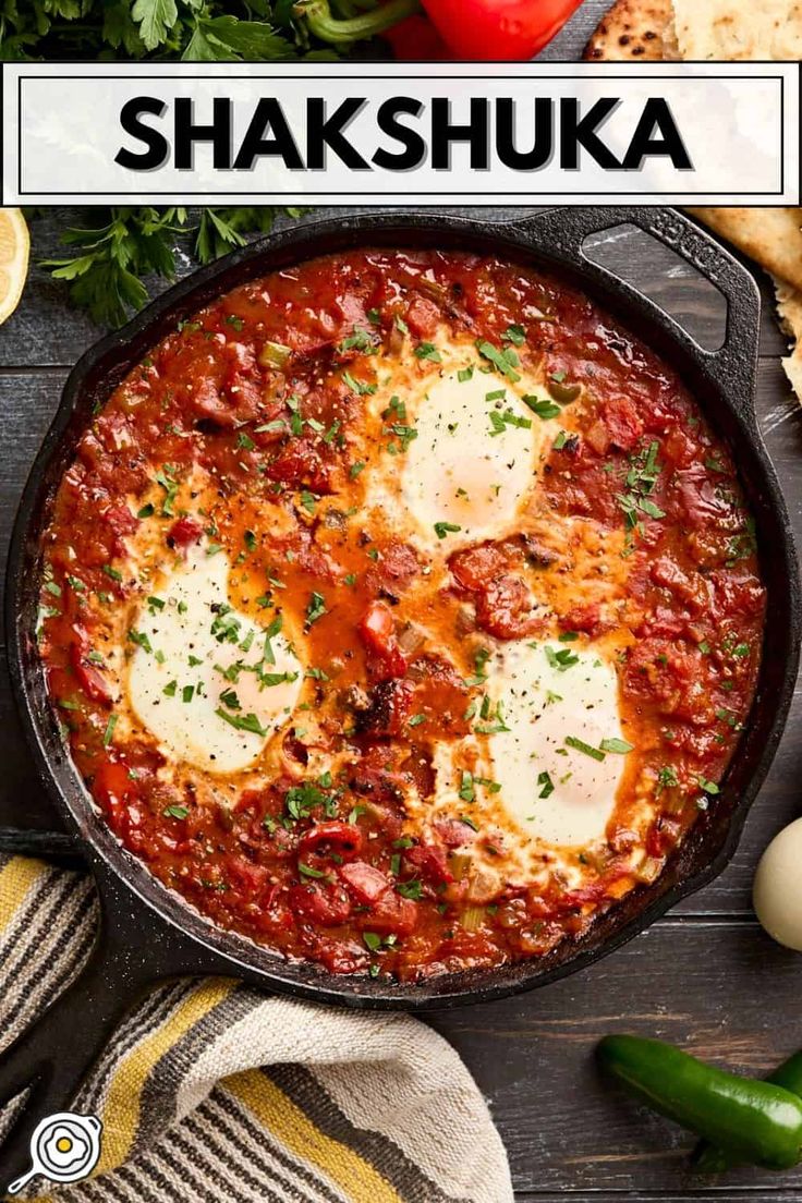 a skillet filled with eggs and sauce on top of a wooden table next to bread