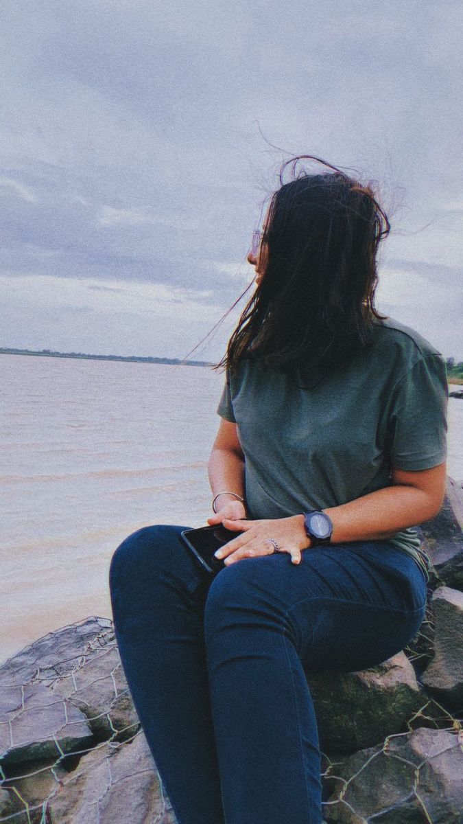 a woman sitting on top of a rock next to the ocean