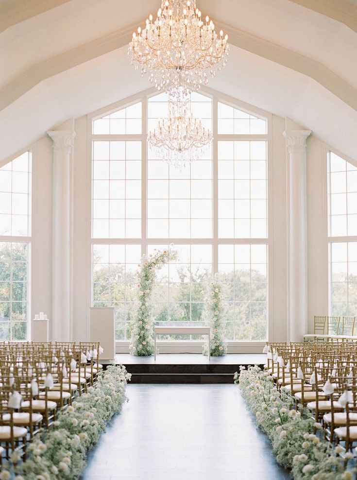 the aisle is decorated with flowers and greenery for an elegant wedding ceremony in front of large windows