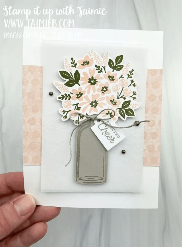 a hand holding up a card with flowers and a tag attached to the front of it