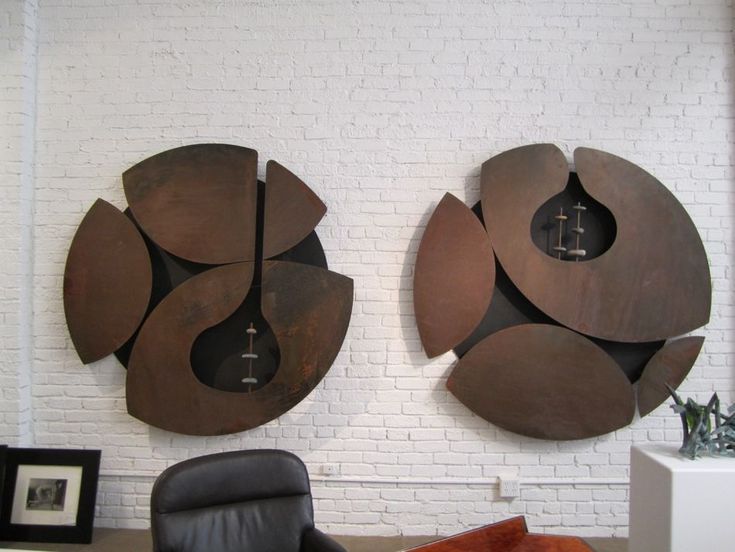 two large metal sculptures on the wall next to a black chair and white brick wall