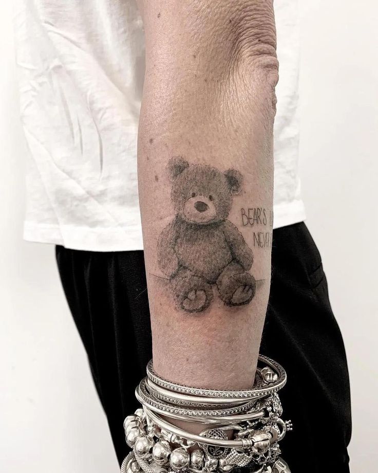 a person with a tattoo on their arm holding onto a bracelet and a teddy bear