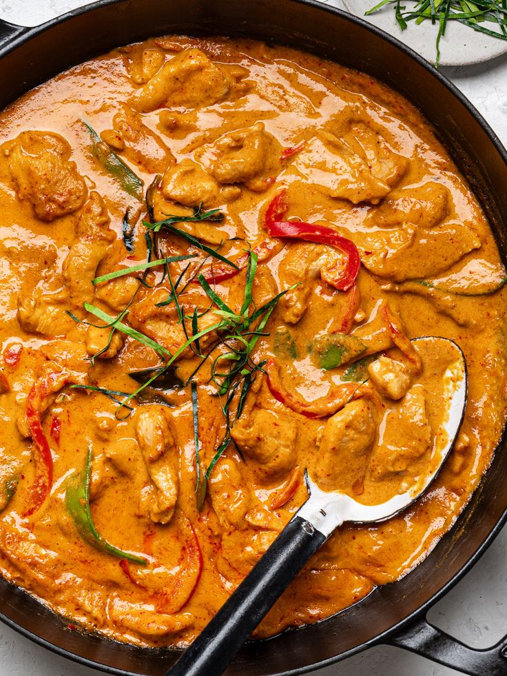 a skillet filled with chicken curry and garnished with red peppers, green onions and carrots