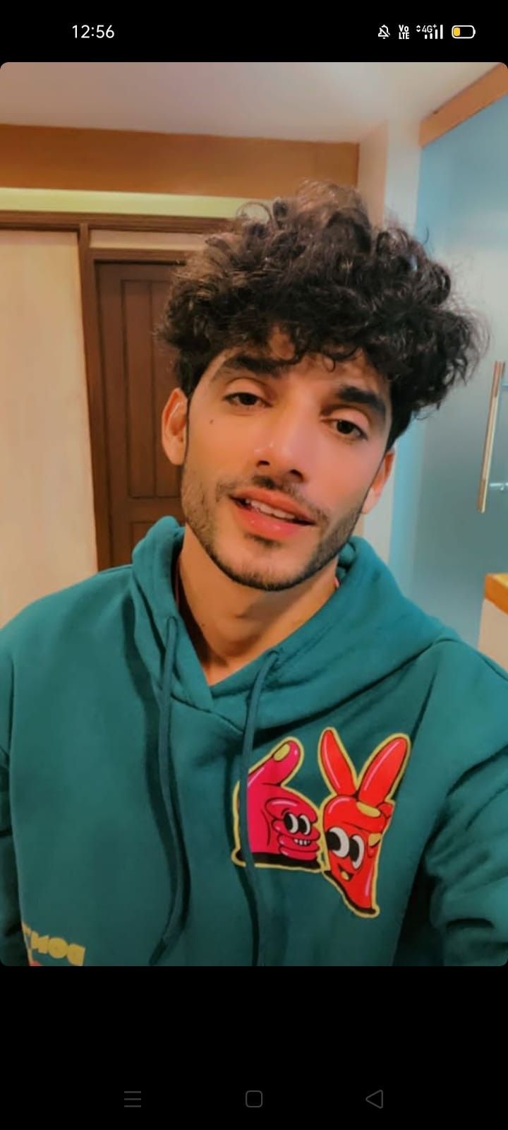 a man with curly hair wearing a green hoodie looking at the camera and smiling