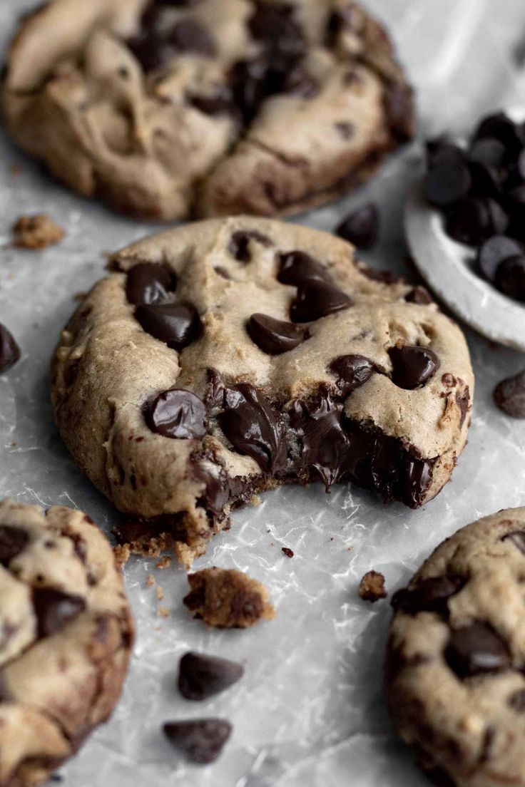 several chocolate chip cookies on a baking sheet with one broken in half and the other partially eaten