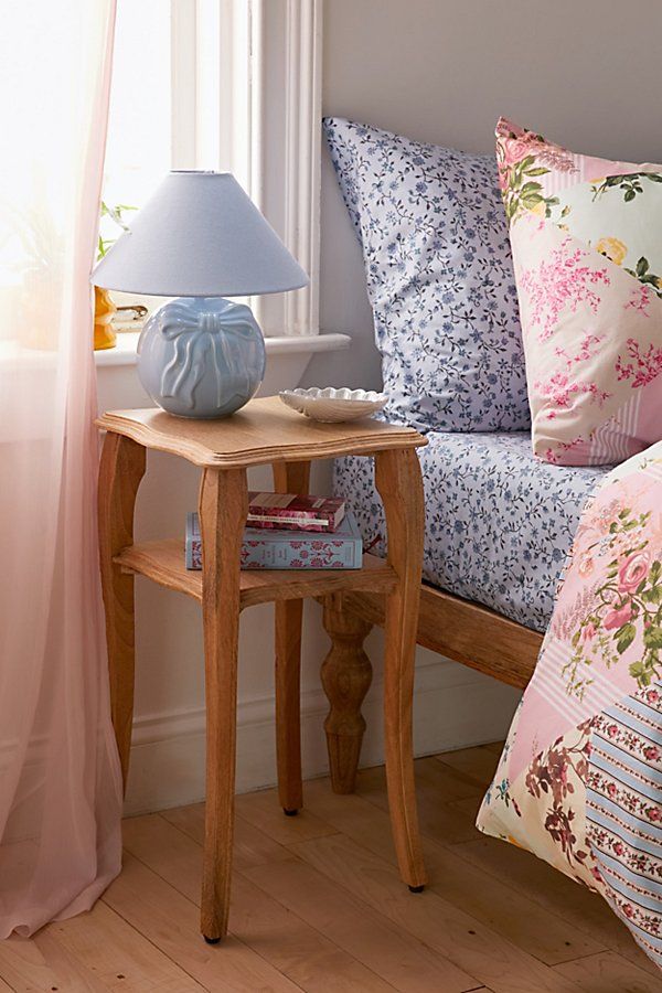 a small table with a lamp on it next to a bed