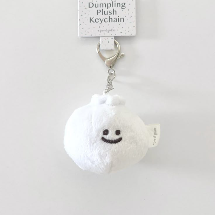 a white stuffed animal keychain with a smiley face hanging from it's side