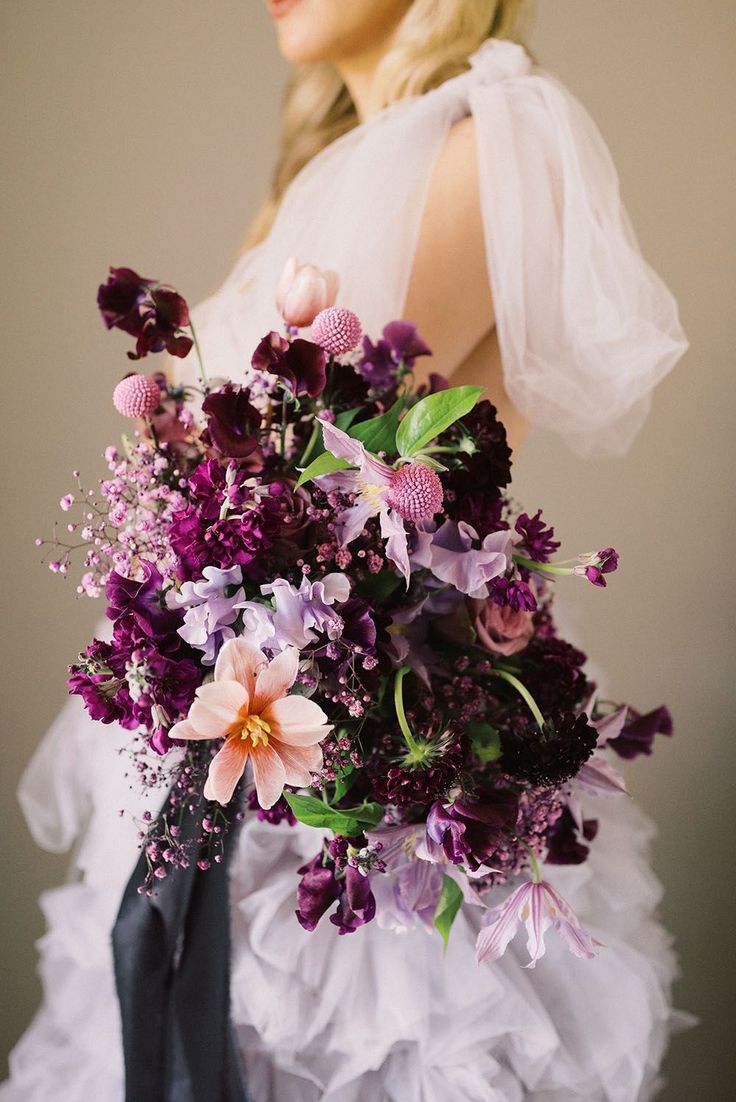 a woman in a white dress holding a bouquet of purple and pink flowers on her wedding day