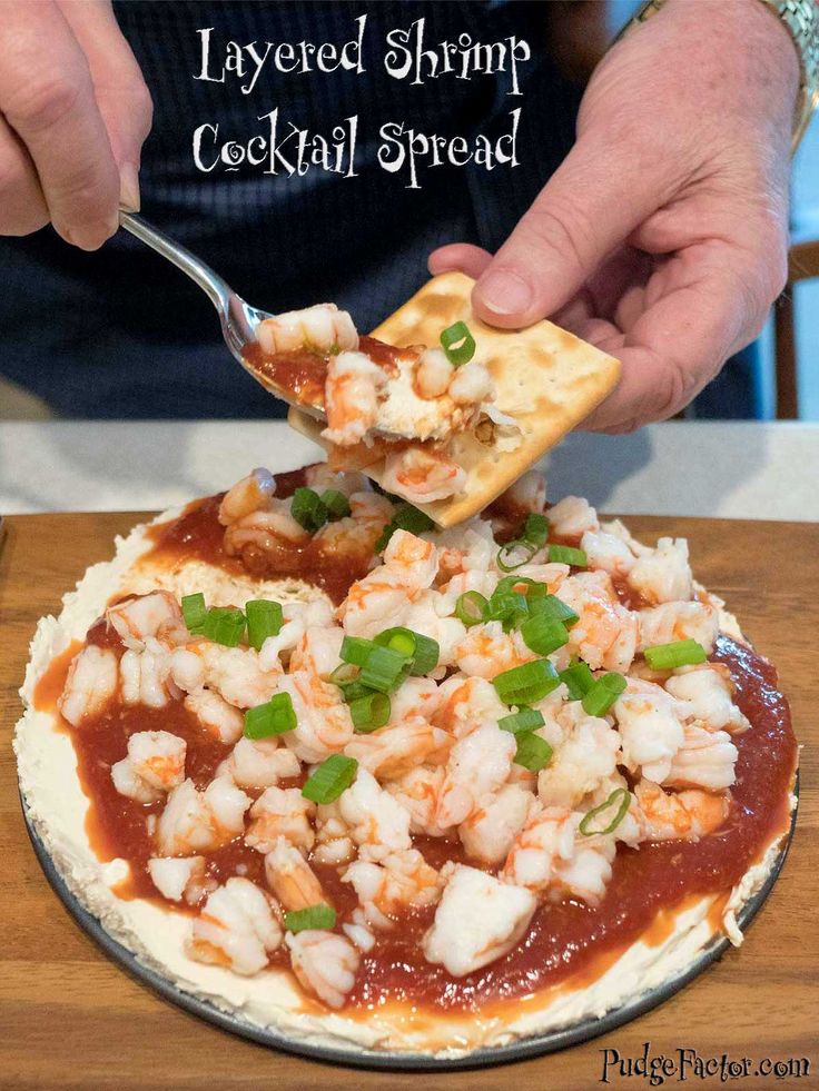 a person is spooning some food out of a small pizza on a plate with the words layered shrimp cocktail spread over it