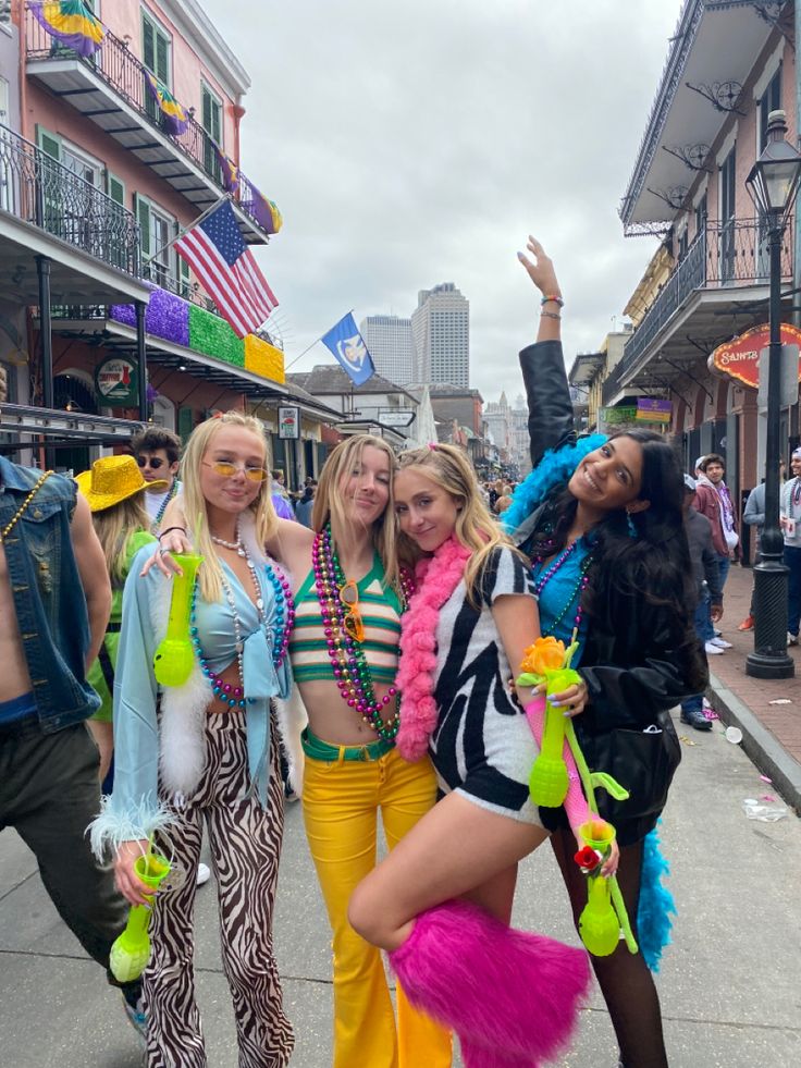 three women dressed in costumes posing for a photo on the street with people standing around